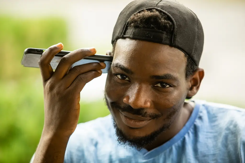 A young man holds his phone up to listen to a message