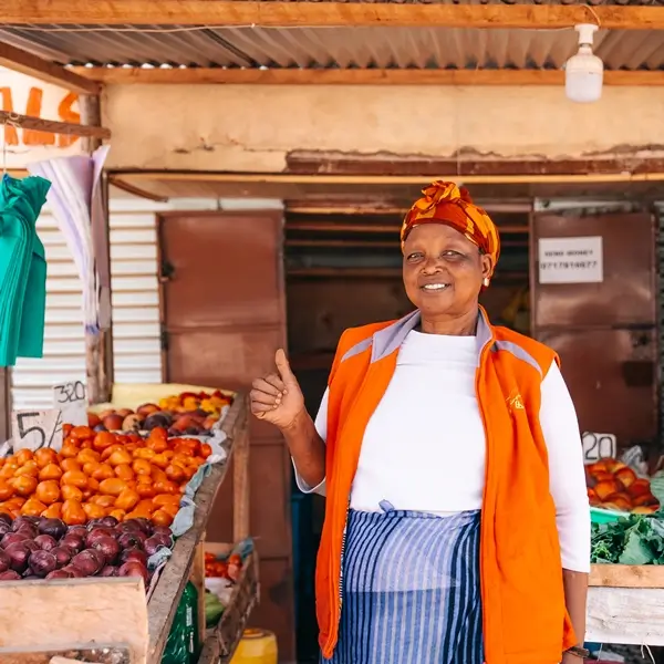 Vegetable seller at her stall, giving the thumbs up after receiving a loan